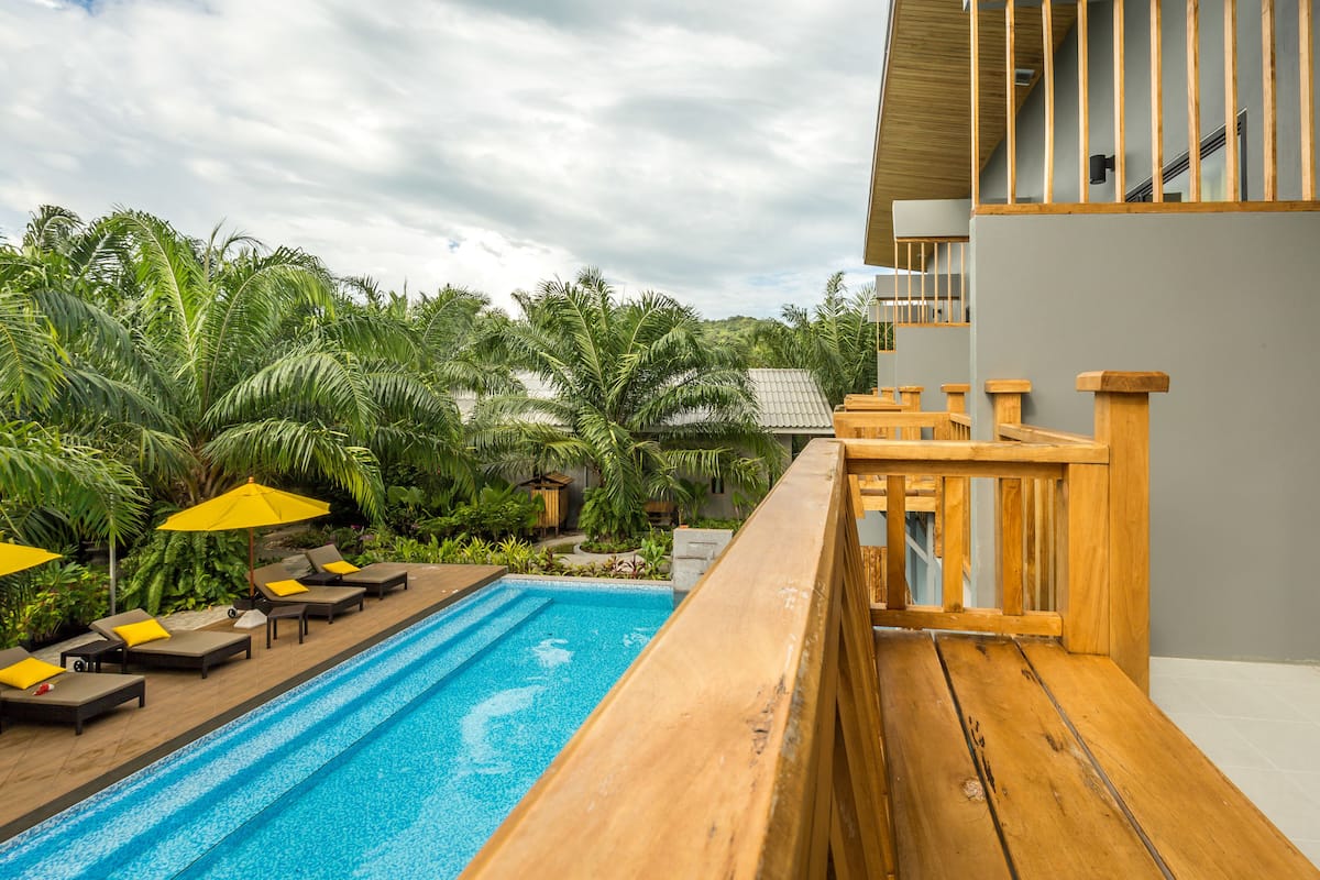 A rooftop pool with wooden railings, sun loungers, and umbrellas.