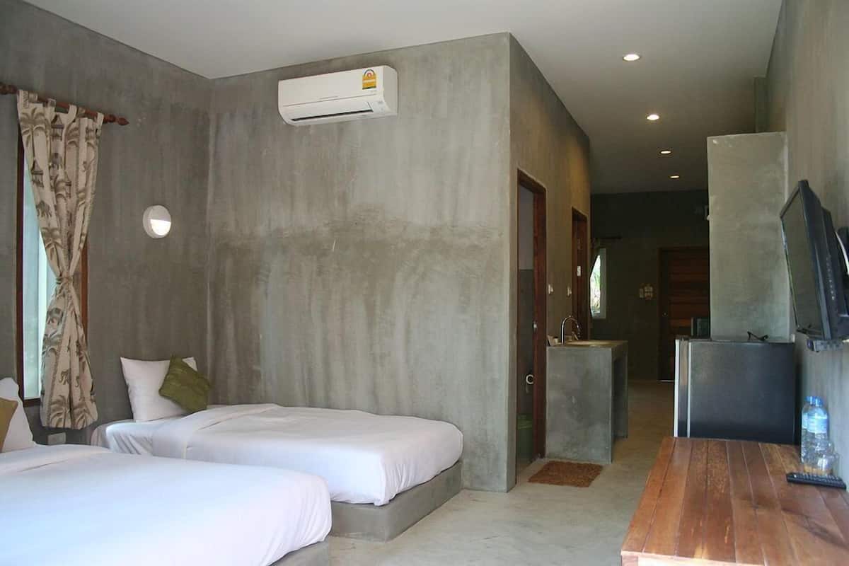 A hotel room with two beds, a wooden table, a TV, and an air conditioning unit.