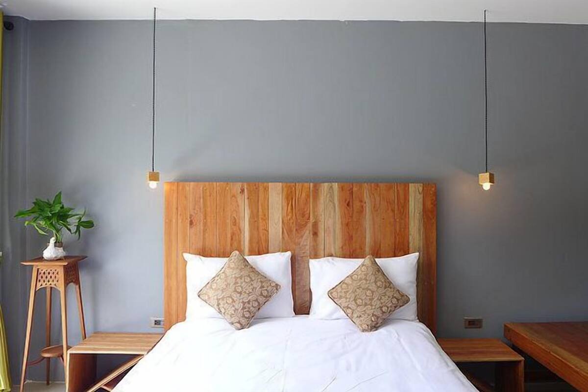 A bedroom with a wooden headboard, two white pillows, a bedside table, and a potted plant.