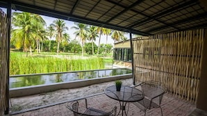 A covered outdoor area with a view of a rice field and palm trees, featuring two metal chairs and a small table. - Cha-Am Country Home (Cha-am)