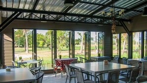 An open-plan dining area with large windows, tables, and chairs. - Cha-Am Country Home (Cha-am)