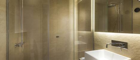 Un baño moderno con ducha de vidrio, lavabo blanco y un espejo grande.