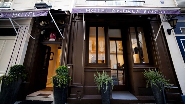 The entrance of Hotel Andrea Rivoli with a dark brown facade, large windows, and potted plants at the entrance. - Hotel Andrea (Paris)