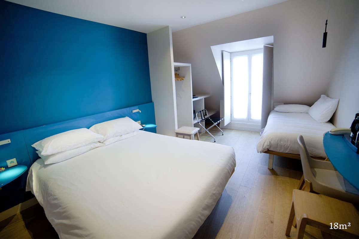 A hotel room with a large bed, a smaller bed, a desk, a chair, and a window.