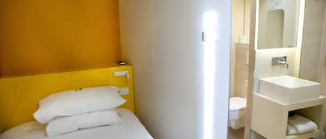 Una habitación de hotel con cama, baño con lavamanos y espejo, y ducha.