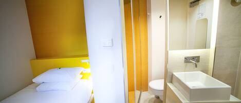 Una habitación de hotel con cama, baño con lavamanos y espejo, y ducha.