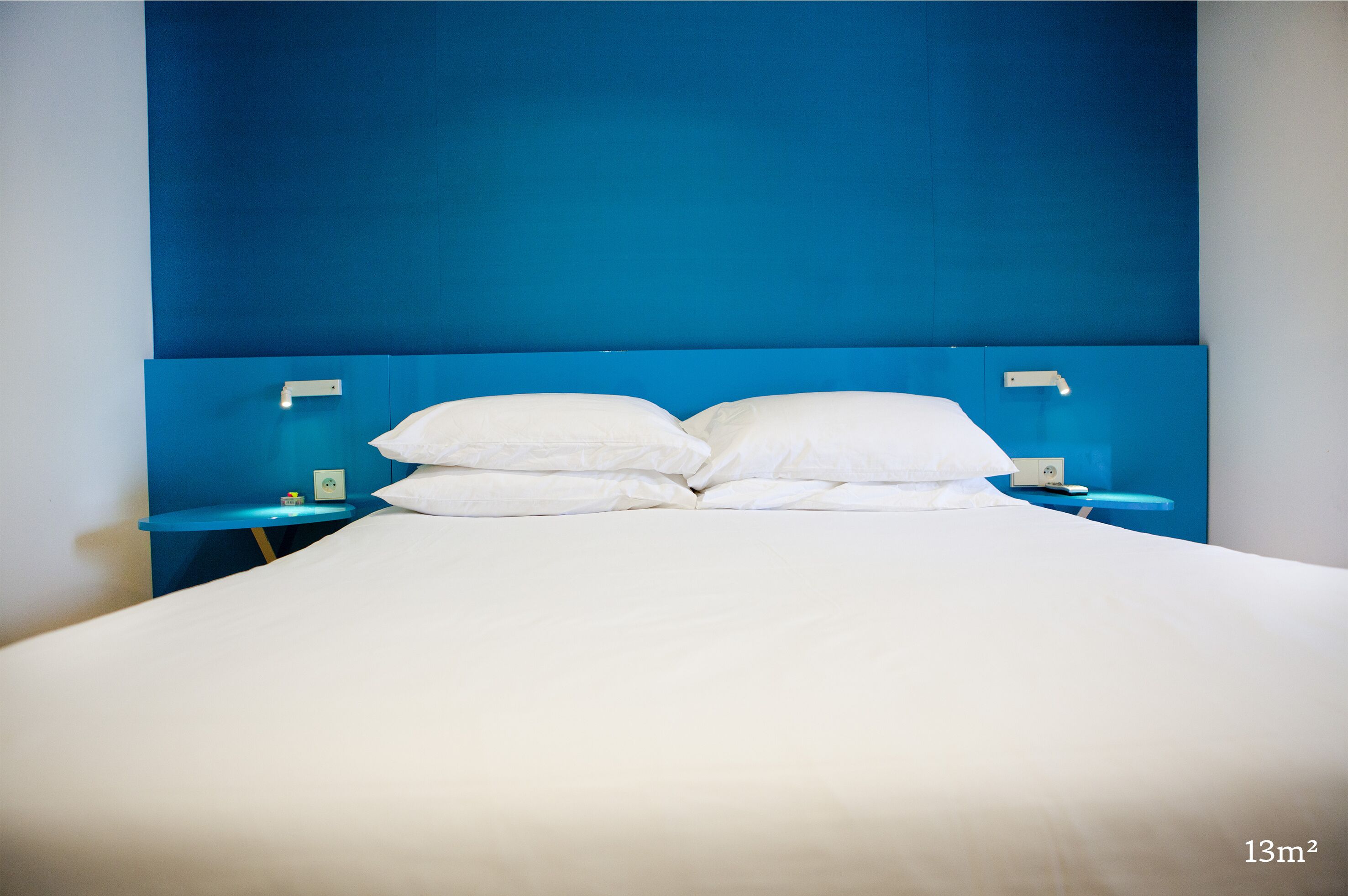 A bed with white bedding, a blue headboard, and two bedside tables with lamps.