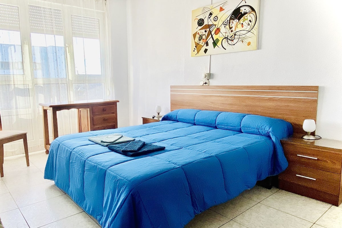 A bedroom with a bed, a desk, a chair, and a painting on the wall.