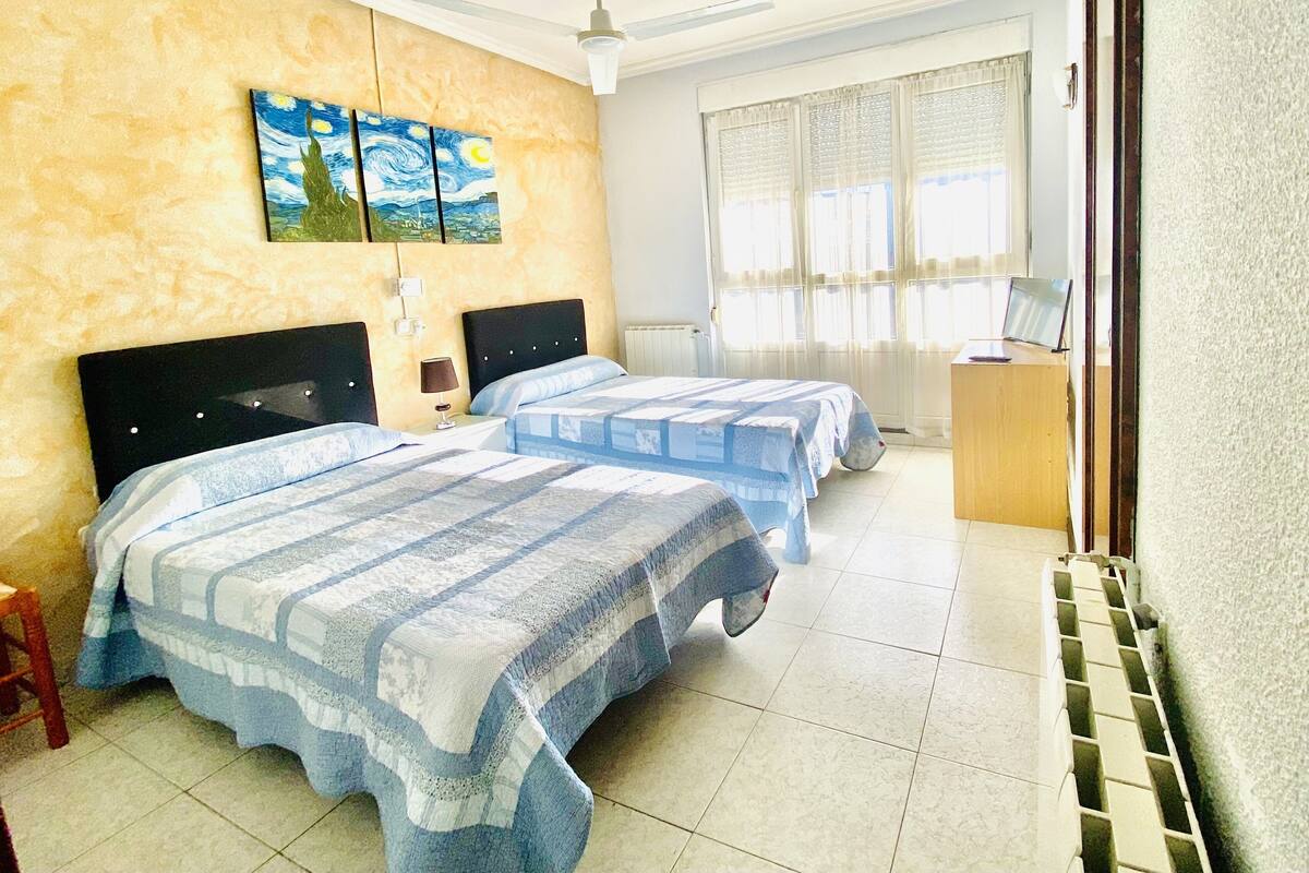 A hotel room with two beds, a painting on the wall, a desk, and a radiator.
