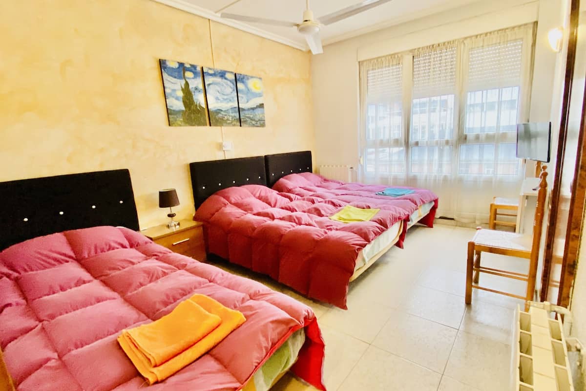 A hotel room with three beds, a small table, and a chair.