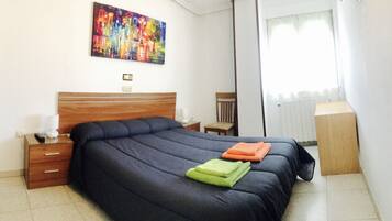 Een netjes opgemaakt slaapkamer met een groot bed, een nachtkastje met een lamp, een stoel en een radiator.