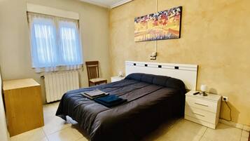 Ein Schlafzimmer mit Bett, Nachttisch, Sessel, Heizkörper und einem Gemälde an der Wand.