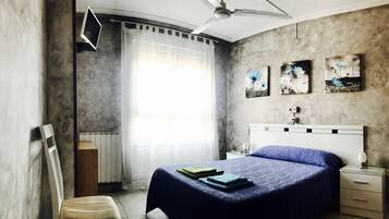 A bedroom with a bed, a nightstand, a chair, a ceiling fan, and artwork on the wall.
