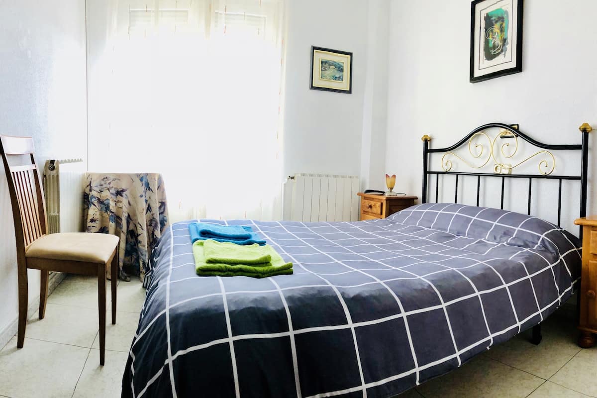 A bedroom with a bed, a chair, a nightstand, and a radiator.