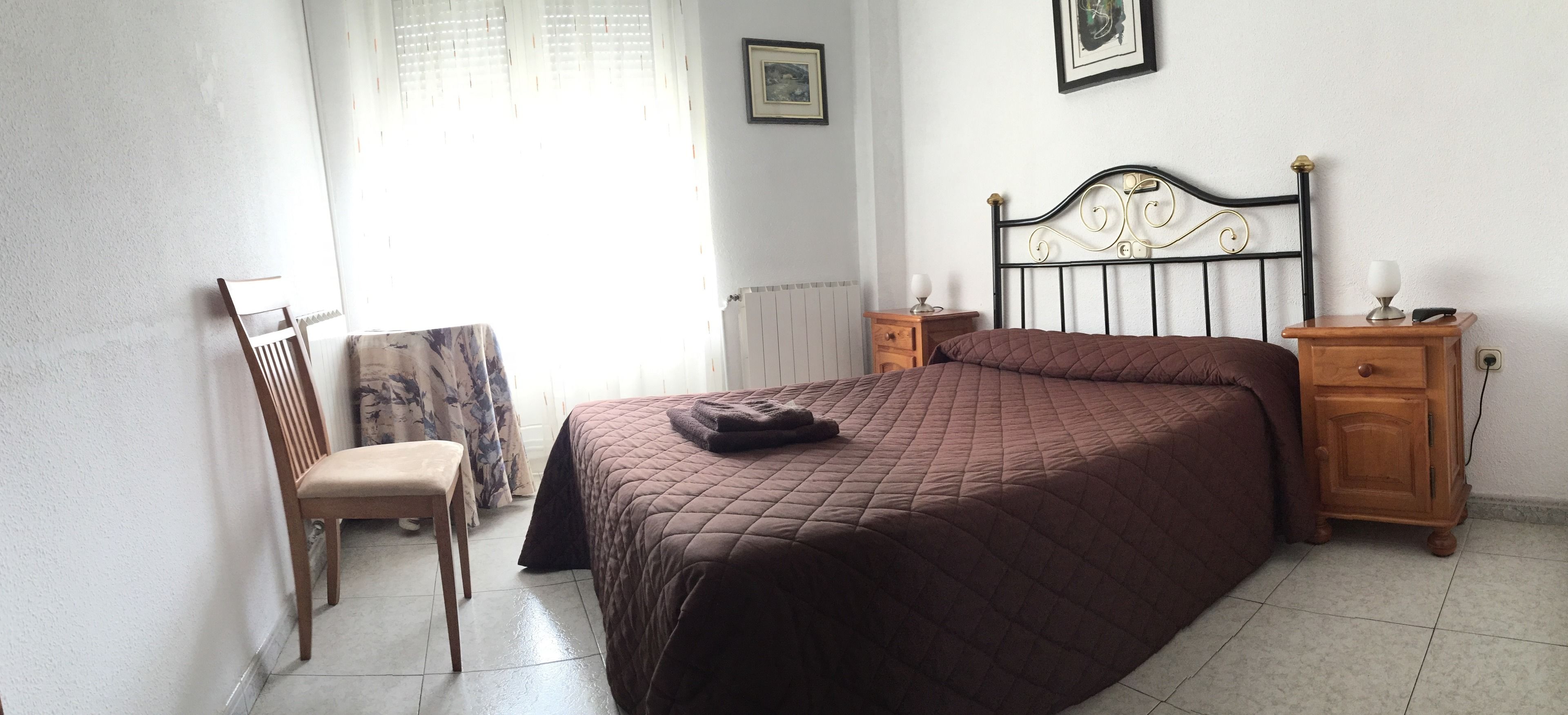Un dormitorio con una cama, una silla, una mesita de noche y un radiador.