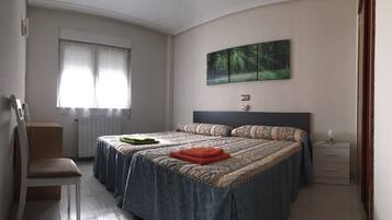 A bedroom with two beds, a radiator, a window with curtains, a painting of a forest, and a bedside table with a lamp.