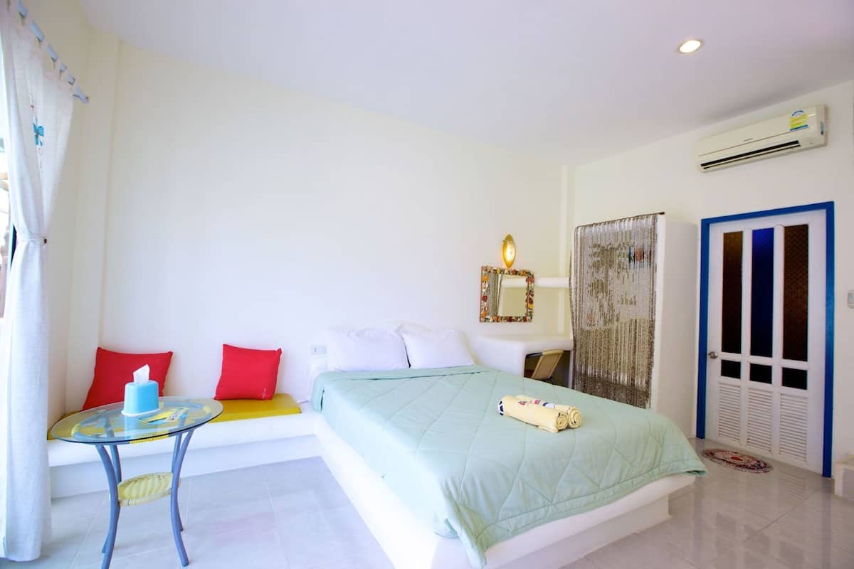 A hotel room with a bed, a small table with a chair, a desk, and a wardrobe.
