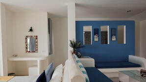 A modern hotel room with a white and blue color scheme, featuring a sofa, a small table, and a mirror with decorative frames. - Anavilla Tangke Resort (Khanom)