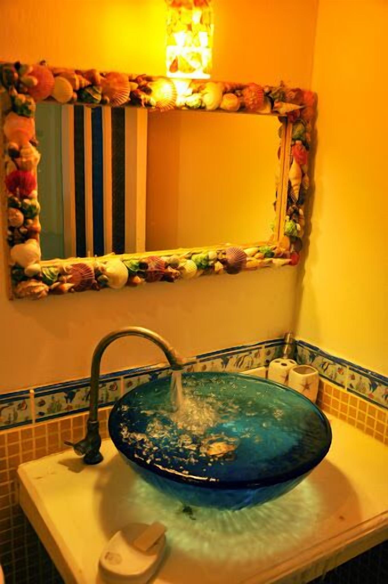 A bathroom with a blue glass sink, a striped mirror frame, and a decorative border.