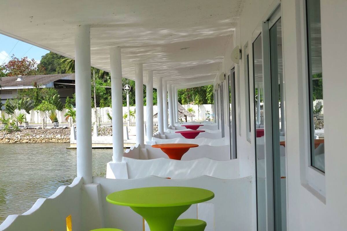 A covered outdoor seating area with white columns, green tables, and red and orange chairs.