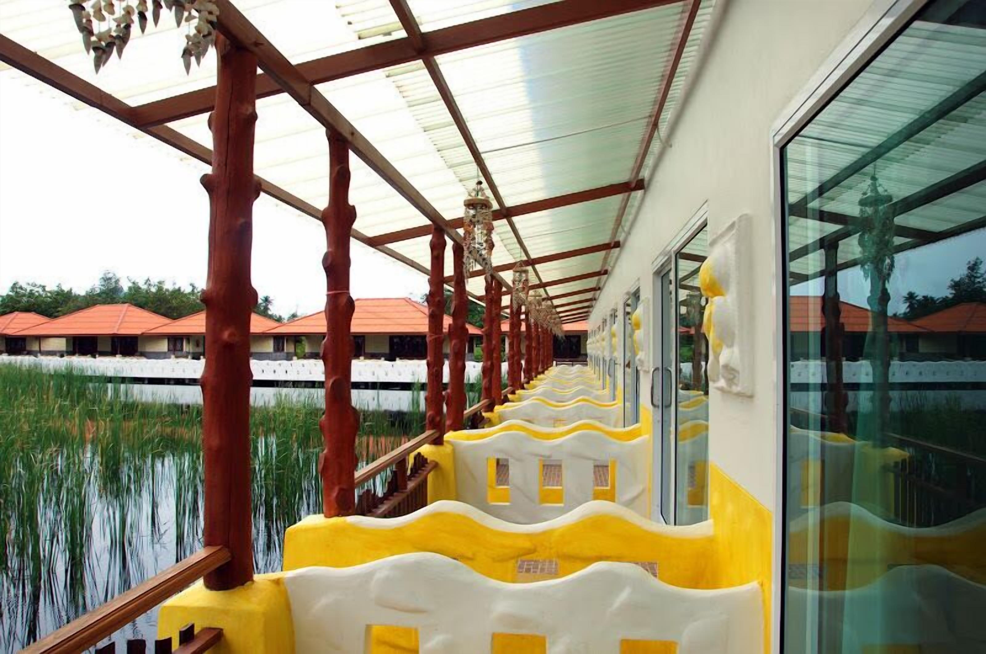 A corridor with a glass wall on one side, wooden pillars, and a yellow and white patterned railing.