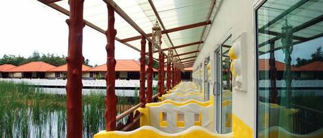 A corridor with a glass wall on one side, wooden pillars, and a yellow and white patterned railing.