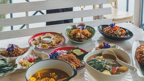 A dining table with various dishes and a person standing by the railing. - Anavilla Tangke Resort (Khanom)