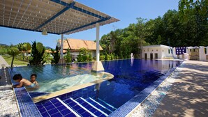 A swimming pool with a tiled edge, a covered area, and a building in the background. - Anavilla Tangke Resort (Khanom)