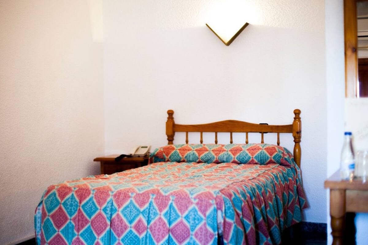 Un lit simple avec une tête de lit en bois, une couvre-lit à motifs et une table de chevet avec une lampe.