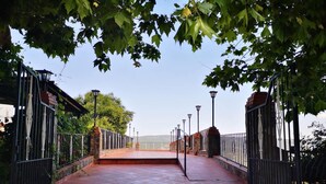 A stone pathway leading to a gated entrance with metal railings and street lamps.