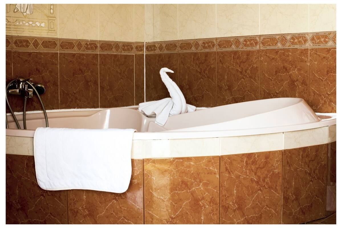 Une baignoire avec une serviette, une pomme de douche et une bordure décorative en carreaux.