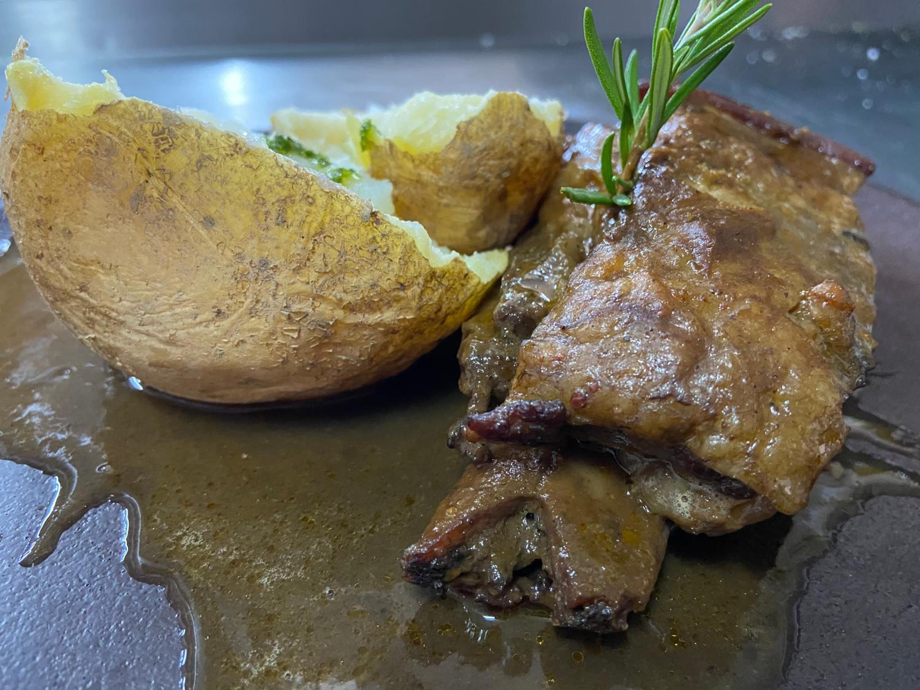 Un plato con carne asada y una patata grande.