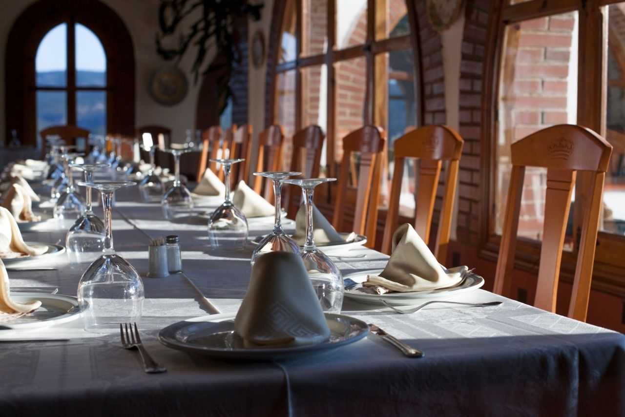 Una larga mesa de comedor con sillas, vasos transparentes y platos listos para una comida.
