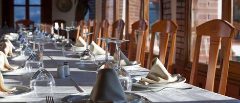 Una larga mesa de comedor con sillas, vasos transparentes y platos listos para una comida.