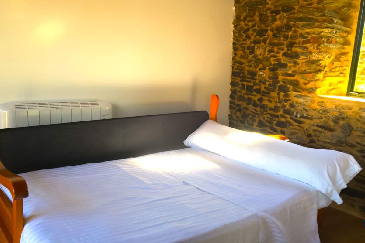 Een eenpersoonsbed met witte lakens in een kamer met een stenen muur en een raam.