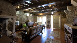 Un interior rústico con paredes de piedra, vigas de madera, chimenea, un sofá y un televisor.