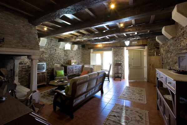 A rustic interior with stone walls, wooden beams, a fireplace, a sofa, and a television. - Vila Peregrina (Arzua)