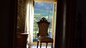 Vista desde una habitación con un ventanal grande, una silla de madera y una pared de piedra.