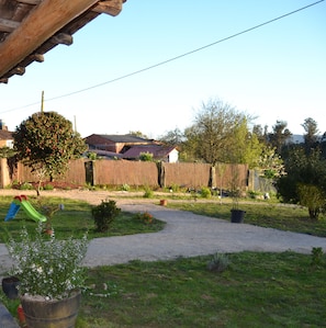Un patio trasero con una terraza de madera, un tobogán verde y una variedad de plantas en macetas.