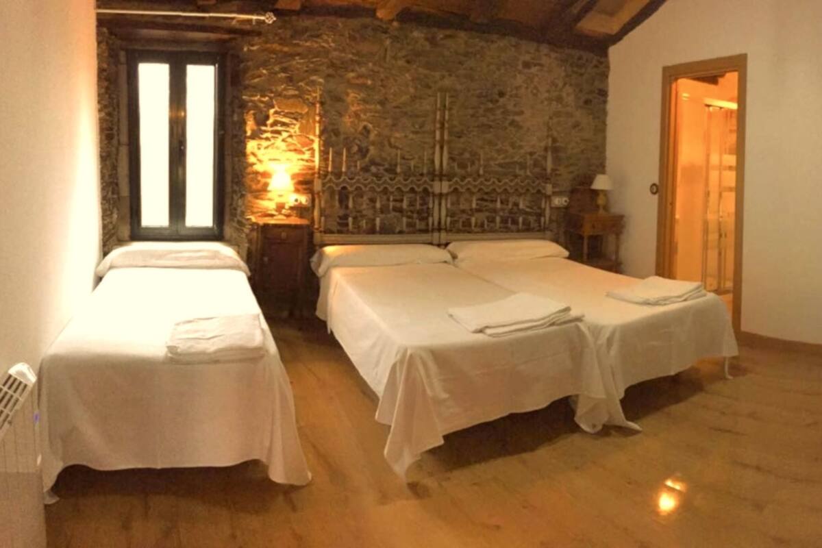 Een kamer met twee eenpersoonsbedden en een groter bed, stenen muren, houten vloeren en een deur naar een andere kamer.
