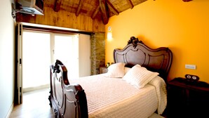 Un dormitorio con techo de madera, una cama con cabecera, una mesita de noche y una lámpara fijada a la pared.