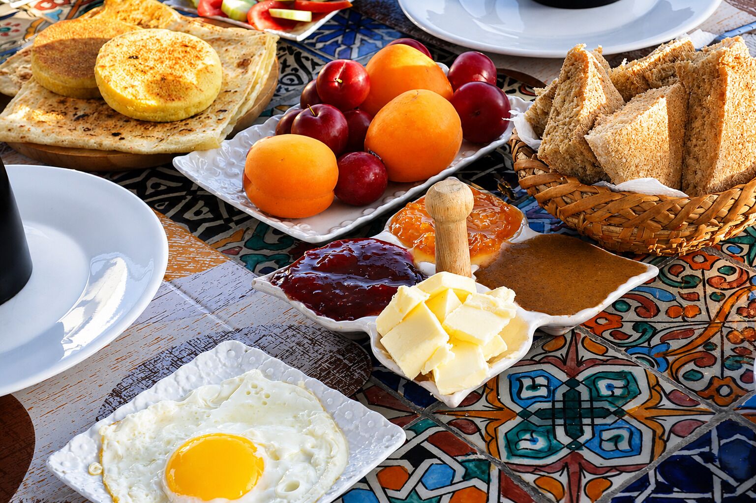 A breakfast table with toast, eggs, fruit, jam, butter, and bread.