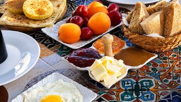 A breakfast table with toast, eggs, fruit, jam, butter, and bread.