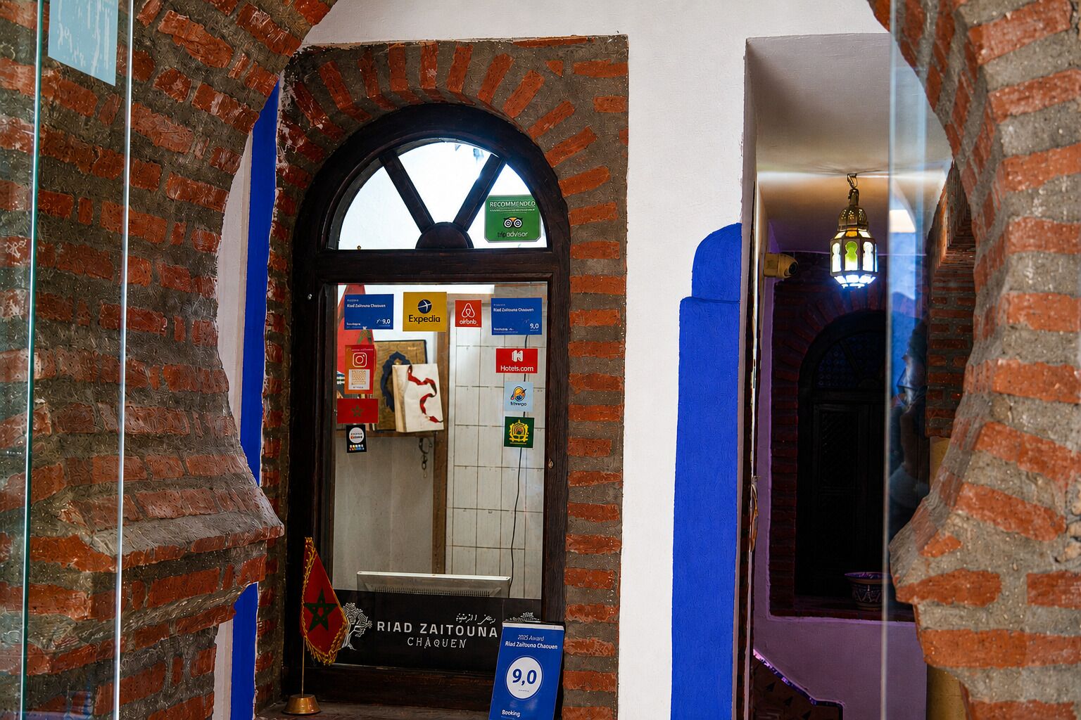 A hotel entrance with a brick archway, a sign indicating a 9.0 rating, and various logos of travel agencies and hotels.