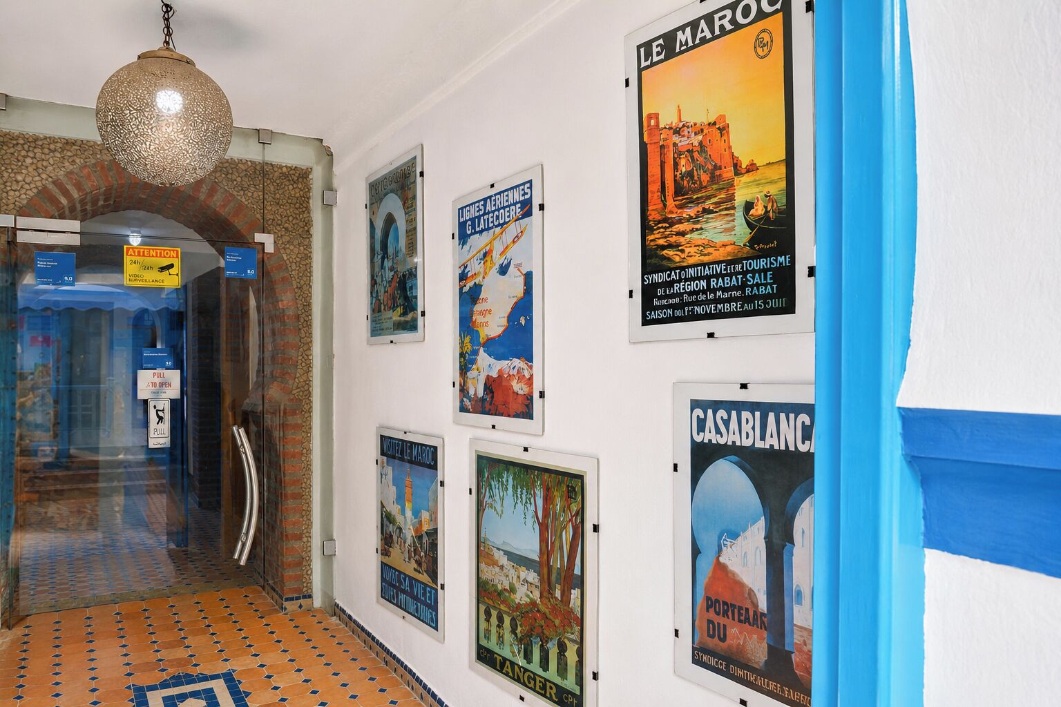 A hallway with a tiled floor, a hanging light fixture, and several posters on the wall.