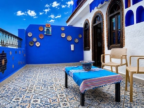 Une terrasse dallée de carreaux bleus, avec une table et des chaises, des assiettes décoratives et une porte dotée d’une fenêtre.