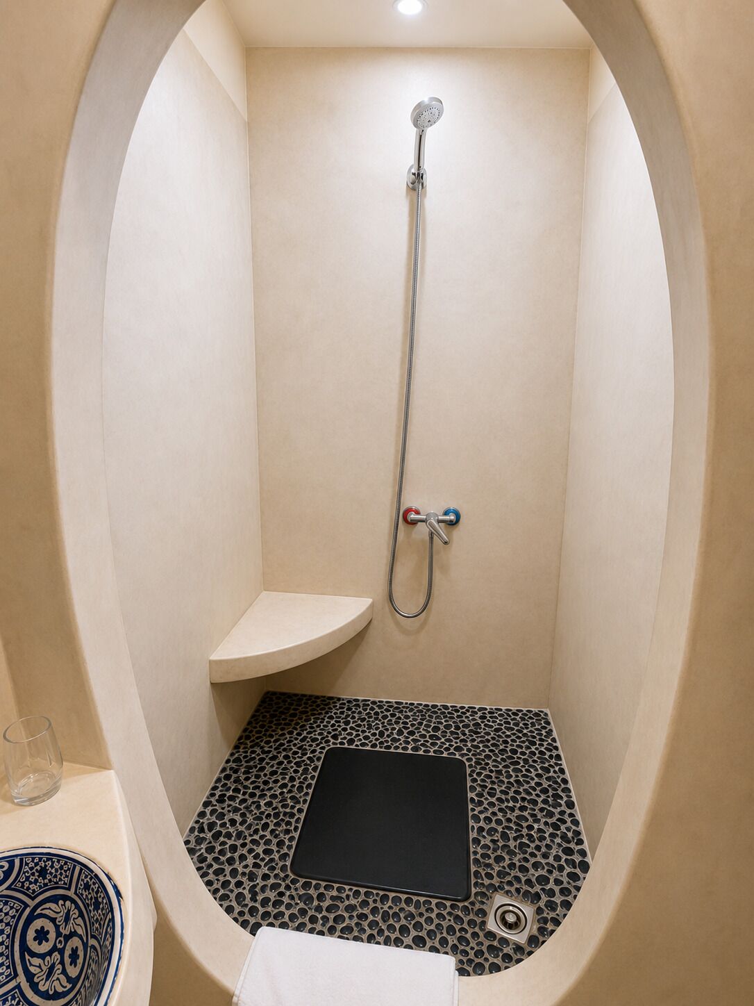 Un baño pequeño y moderno con ducha de mano, lavamanos compacto y un tapete negro en el suelo.