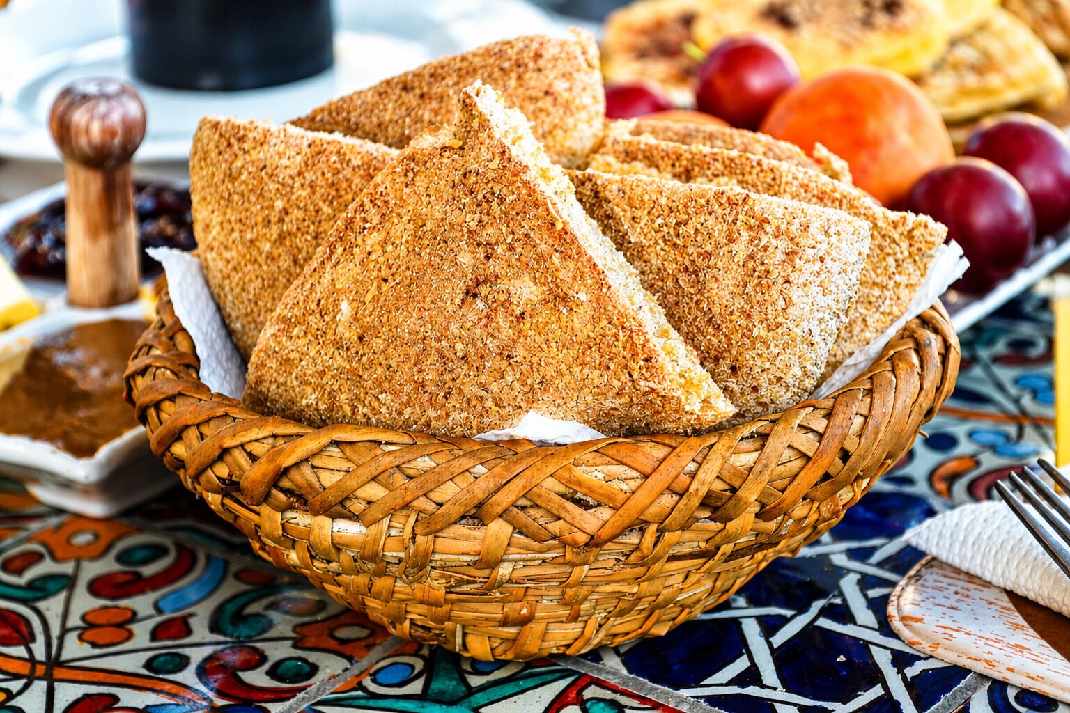 Ein geflochtener Korb mit Brot, ein Holzpfeffermahlwerk und ein Teller mit Obst.