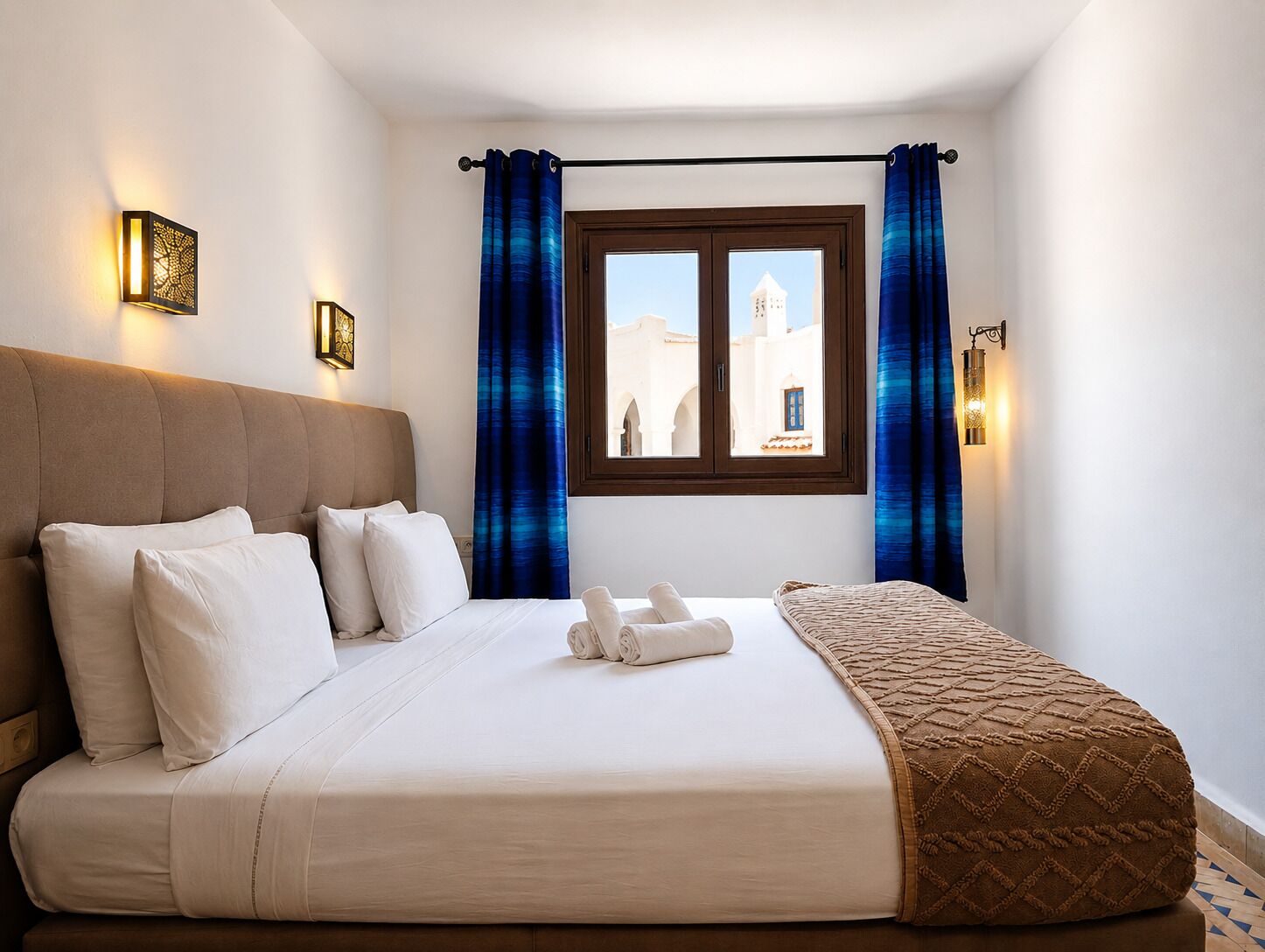Habitación de hotel con cama, almohadas, vista de un edificio a través de la ventana y una barra para cortinas.