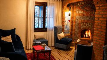 Una habitación acogedora con chimenea, un sofá, una silla y una mesita con un libro rojo.